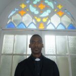 Pastor standing inside a church with stained glass windows, showcasing faith and tradition.
