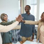 A joyful group of diverse colleagues high-fiving each other in an office, symbolizing teamwork and collaboration.