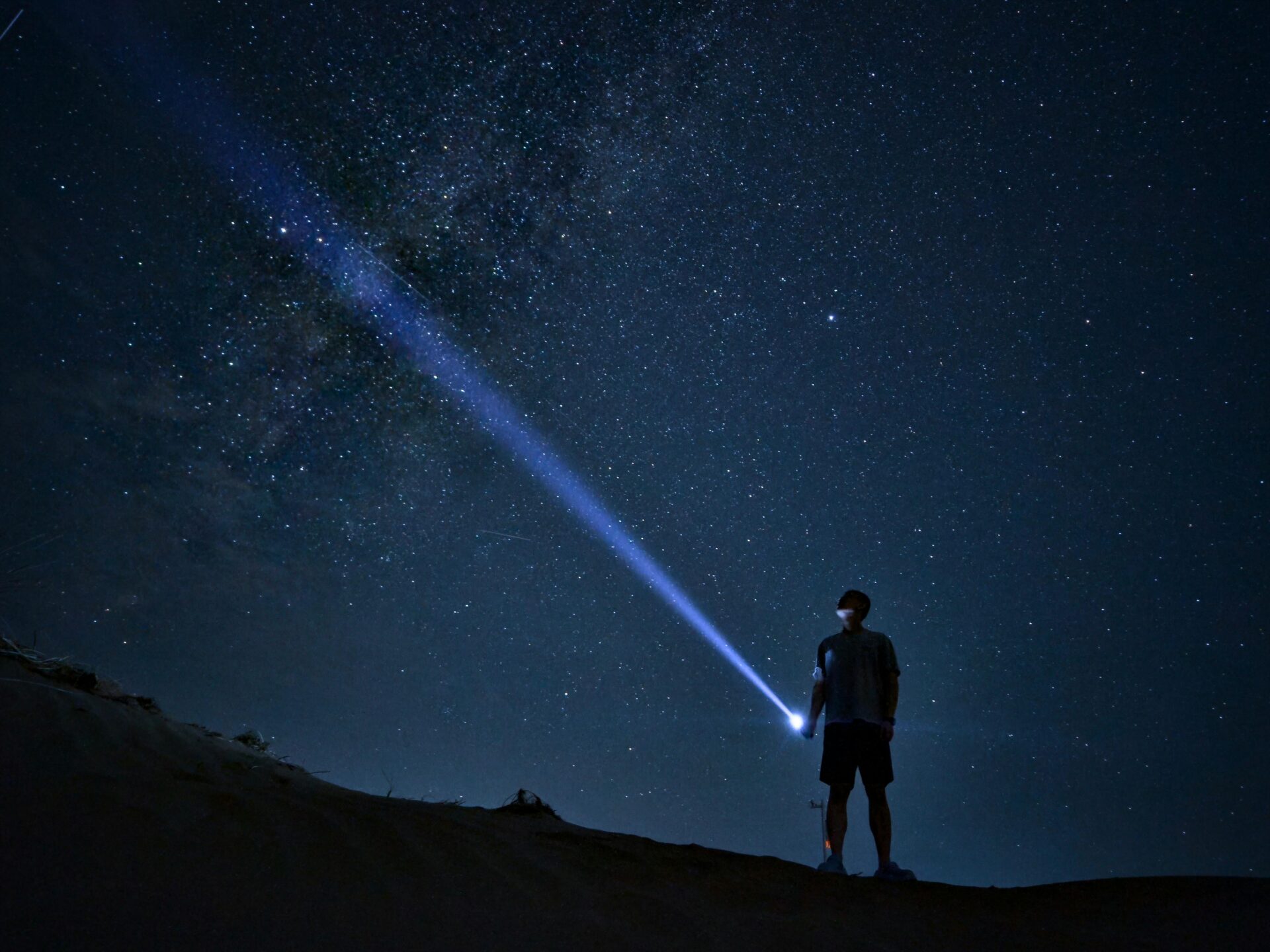 Silhouette of man shining flashlight among stars and dark night sky, embracing exploration.
